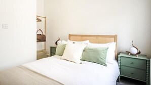 A neatly made bed with a wooden headboard, a green nightstand with drawers, and a mirror with a brown handbag on it. - Newport Ship's Nook (Newport)