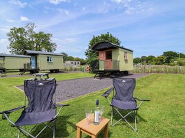 A campsite with two green mobile homes, a gravel path, and two camping chairs.