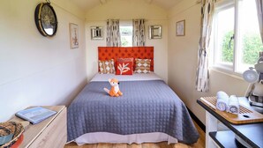 A bedroom with a bed, a nightstand, a window, and a wall clock. - Foxes Den (Whitchurch)
