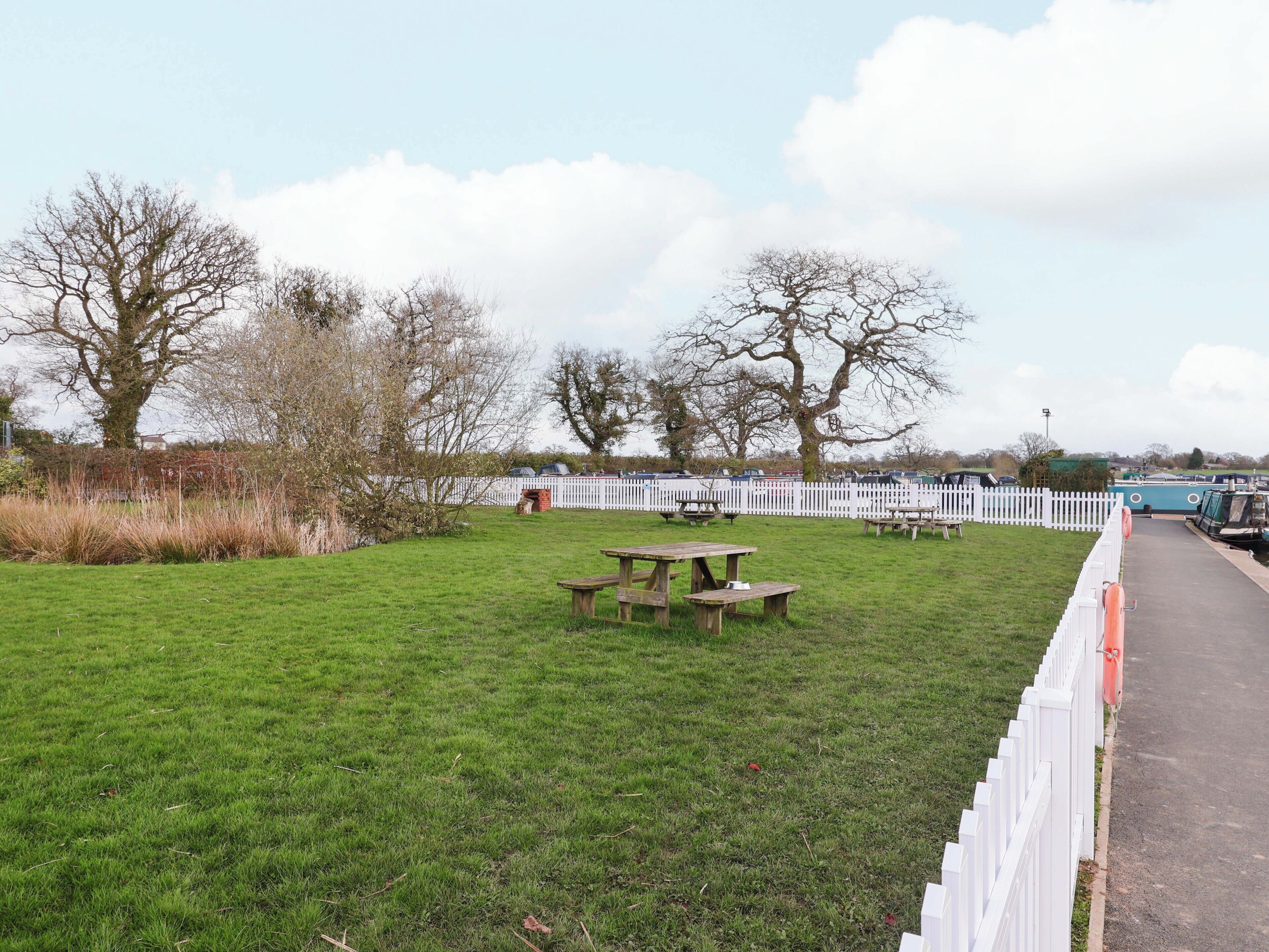 A grassy area with picnic tables and a white fence.