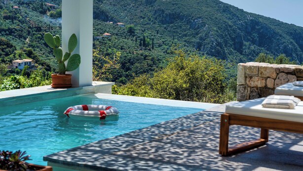 Área da piscina com vista para uma paisagem montanhosa, um cacto em vaso e um muro de pedra.
