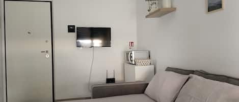 A hotel room with a bed, a TV mounted on the wall, a small table with a radio, and a door with a lock.