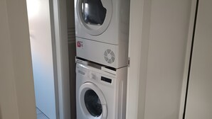 Een wasserette met een gestapelde wasmachine en droger, houten vloeren en witte muren.