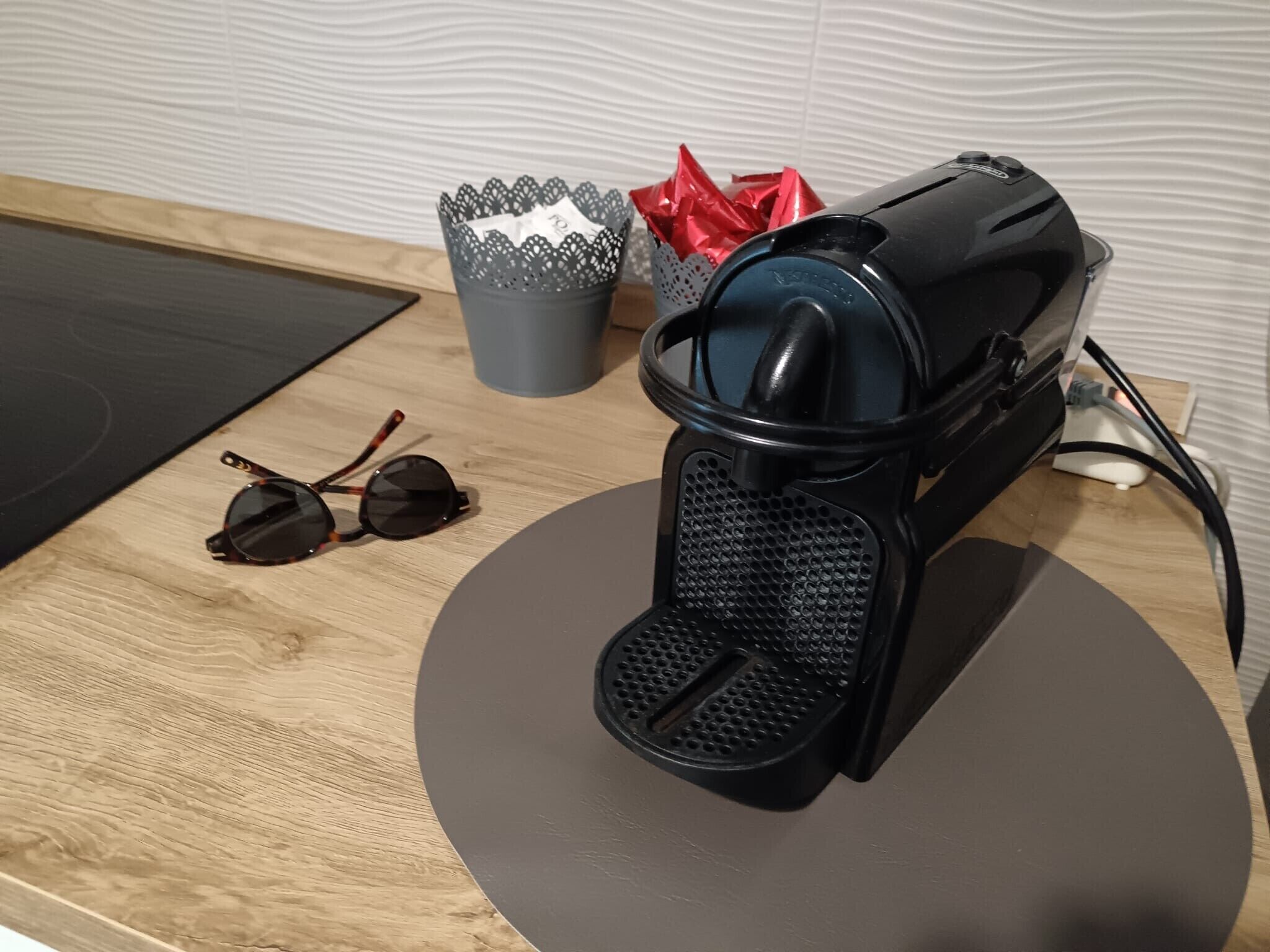 A coffee machine, a pair of sunglasses, and a tissue box on a wooden table.