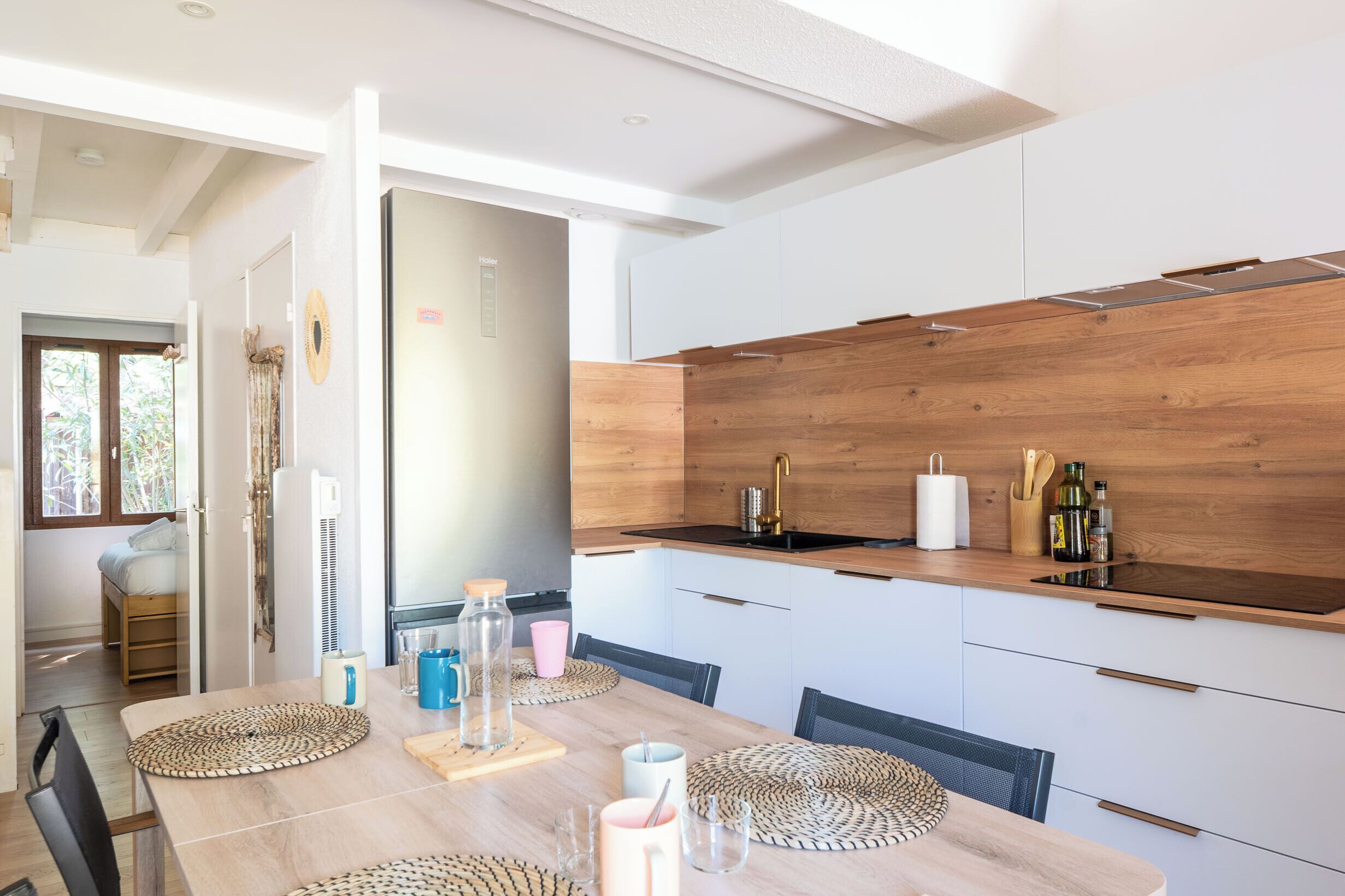 Una cucina moderna con schienale in legno, mobili bianchi e zona pranzo con tavolo in legno e sottopiatti intrecciati.