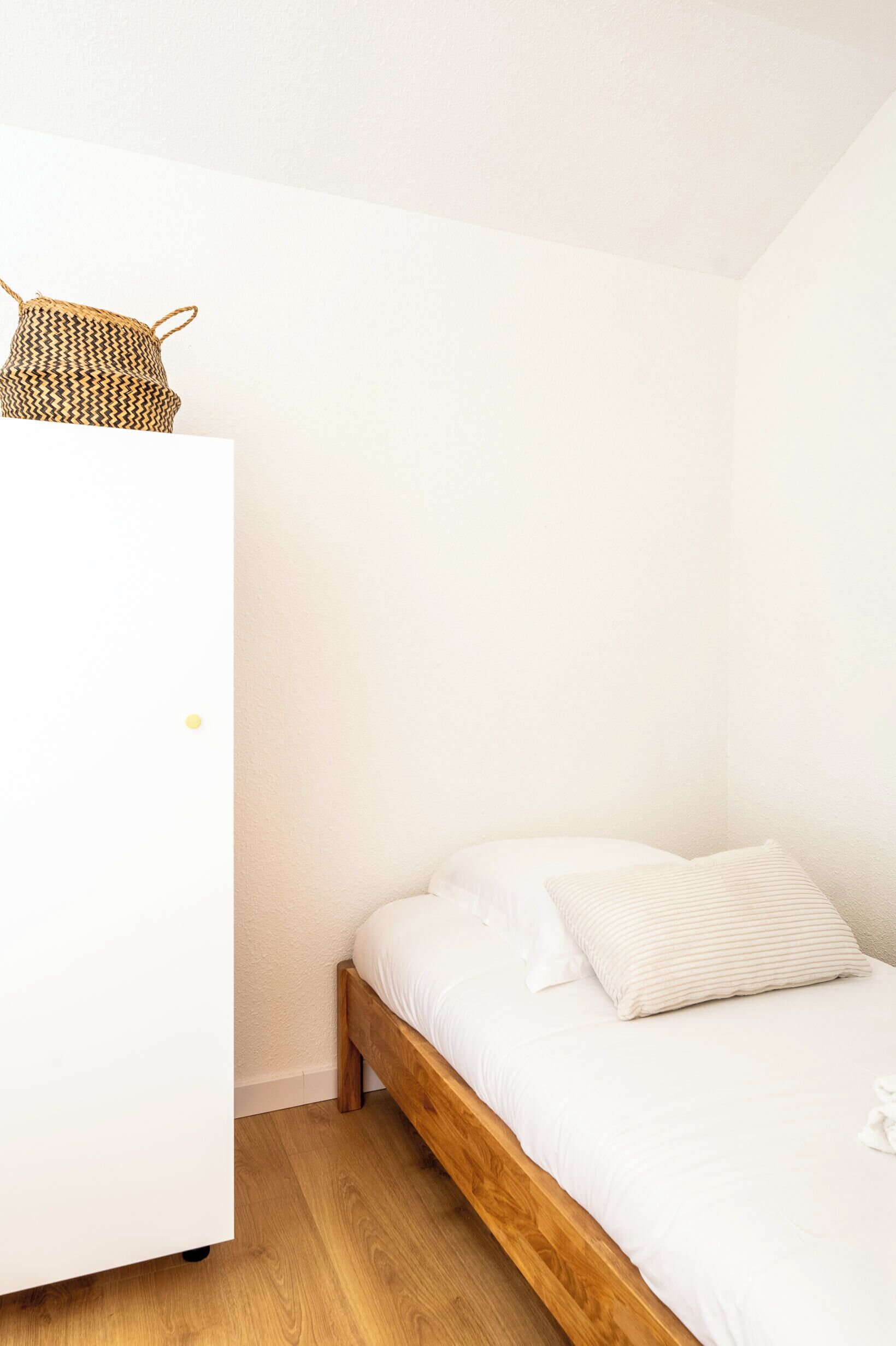 A bedroom with a wooden bed, white bedding, and a woven basket on a white wardrobe.