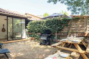 A backyard with a barbecue grill, a dining table set for a meal, and a guitar leaning against a glass door. - House with shared pool in Moliets (Moliets-et-Maa)