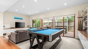 Un salon moderne avec une table de billard, un canapé, un téléviseur et une vue sur le jardin.
