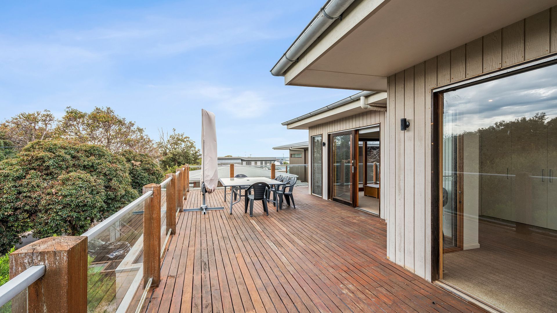Une terrasse en bois avec une table et des chaises, une porte vitrée et une vue sur les arbres.