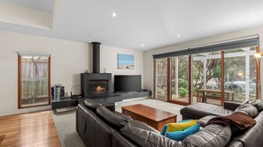Uma sala de estar moderna com lareira, televisão de tela plana e uma grande porta de vidro deslizante que dá para um jardim.