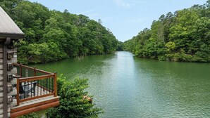 Een rivier omringd door dicht bos, een houten terras met een reling, en een gebouw met een schuin dak.