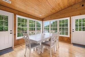 Ein Zimmer mit Holzwänden, einem weißen Tisch und Stühlen, großen Fenstern und einer Tür.