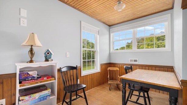 Een kamer met een houten plafond, een tafel, twee stoelen, een boekenplank vol boeken en een raam met uitzicht op groen.