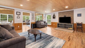A spacious living room with a fireplace, a television, and a large window overlooking a deck.