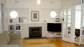 A living room with a fireplace, television, and bookshelves. - Beachside Haven - Point Lonsdale (POINT LONSDALE)