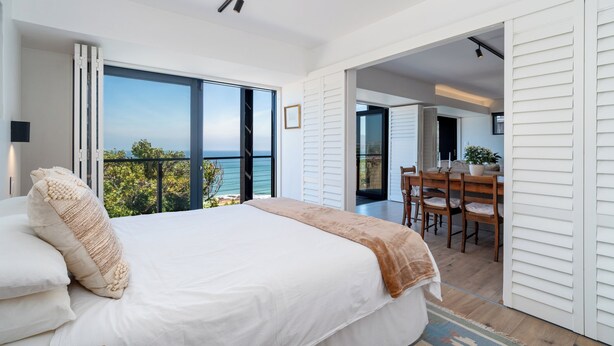 Un dormitorio con una cama grande, vistas al exterior y un comedor con sillas y una mesa.