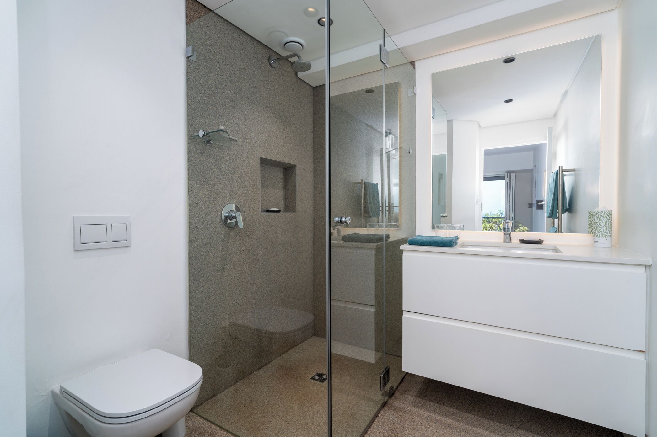 Een moderne badkamer met een douche met glazen wanden, een wit toilet en een wastafel met spiegel.