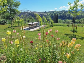 A rustic outdoor dining area with a table and chairs, surrounded by a lush garden with various flowering plants. - Abruzzo Wine & Nature Escape: Cozy Apartment in Bolognano, Italy (Santa Maria del Monte, Pescara)
