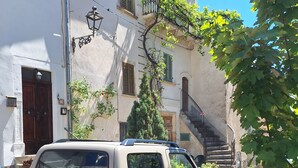 Un SUV color beige estacionado en una calle adoquinada, rodeado de edificios con balcones y un cielo azul despejado.
