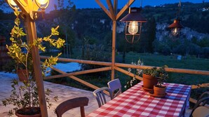 Un patio al aire libre con mantel a cuadros, sillas de madera, plantas en macetas y faroles colgantes.