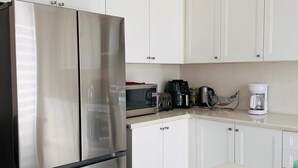 A kitchen with white cabinets, a stainless steel refrigerator, a microwave, a coffee maker, and a toaster. -     The Monarch Residence | Luxury for Families & Groups (Oshawa)