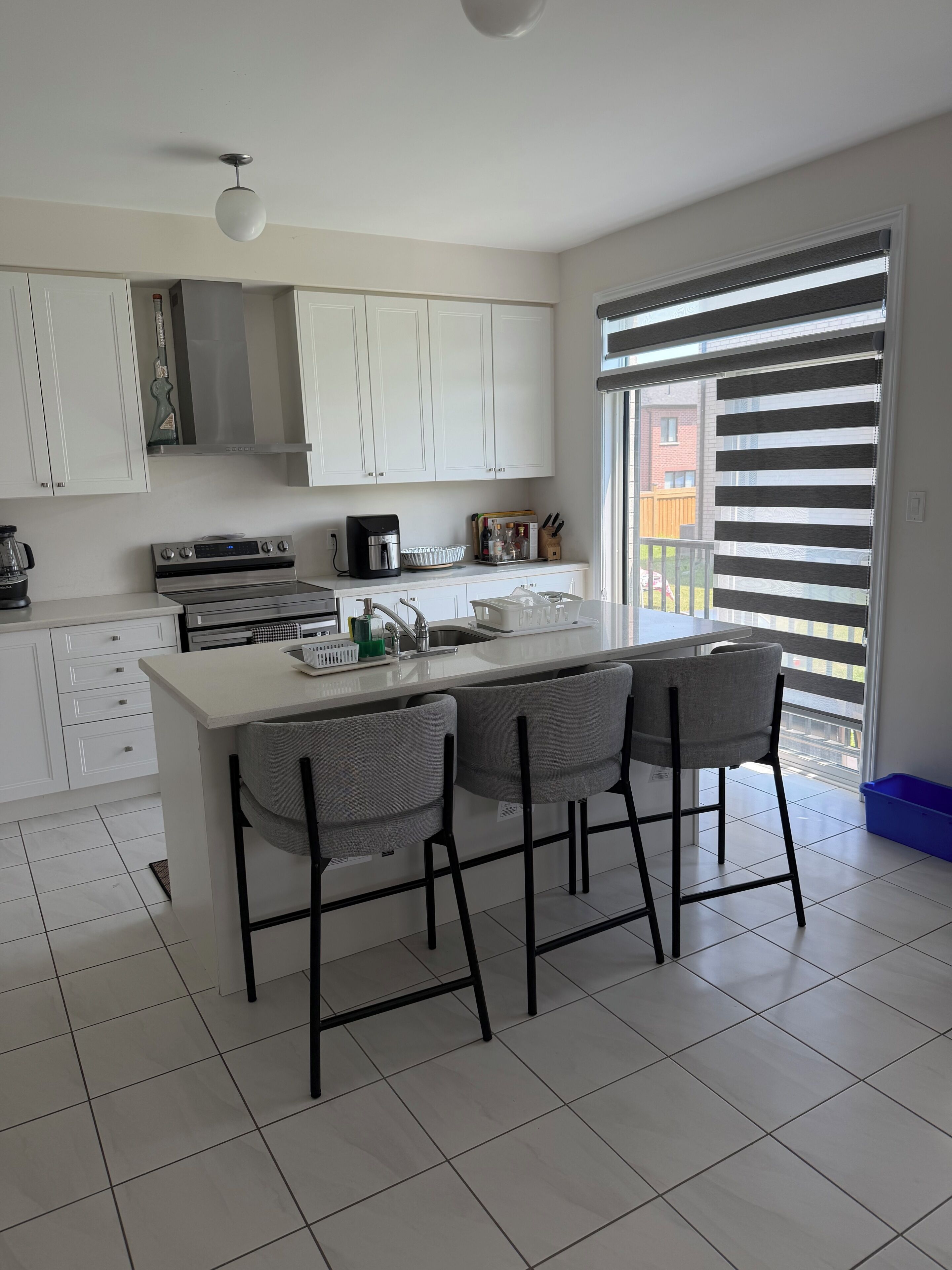 A modern kitchen with white cabinets, a central island with bar stools, a coffee maker, and a view through the window.