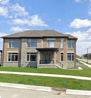 A two-story residential building with a stone facade, multiple windows, and a front porch.