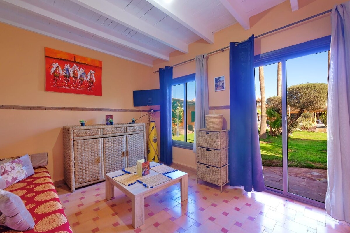 Habitació amb un sofà, una taula, un armari i una finestra gran amb vista a un jardí.
