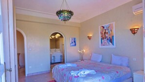 A bedroom with a bed, a chandelier, wall sconces, and a painting.