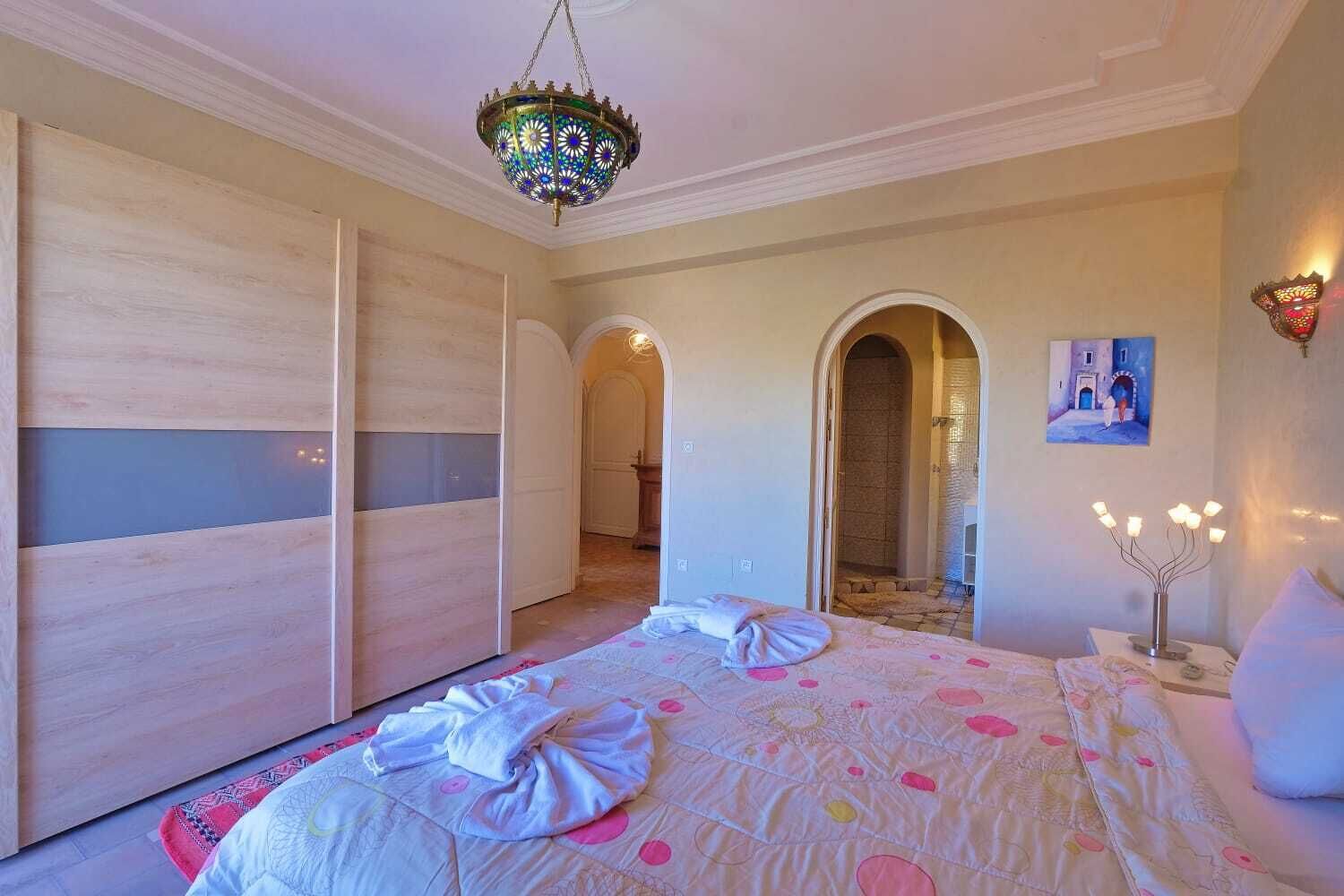 Een slaapkamer met een groot bed, een kroonluchter, een garderobe en een gewelfde deuropening naar een badkamer.