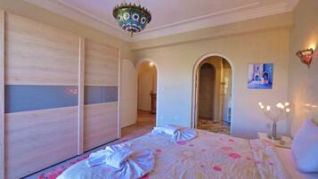 Een slaapkamer met een groot bed, een kroonluchter, een garderobe en een gewelfde deuropening naar een badkamer.