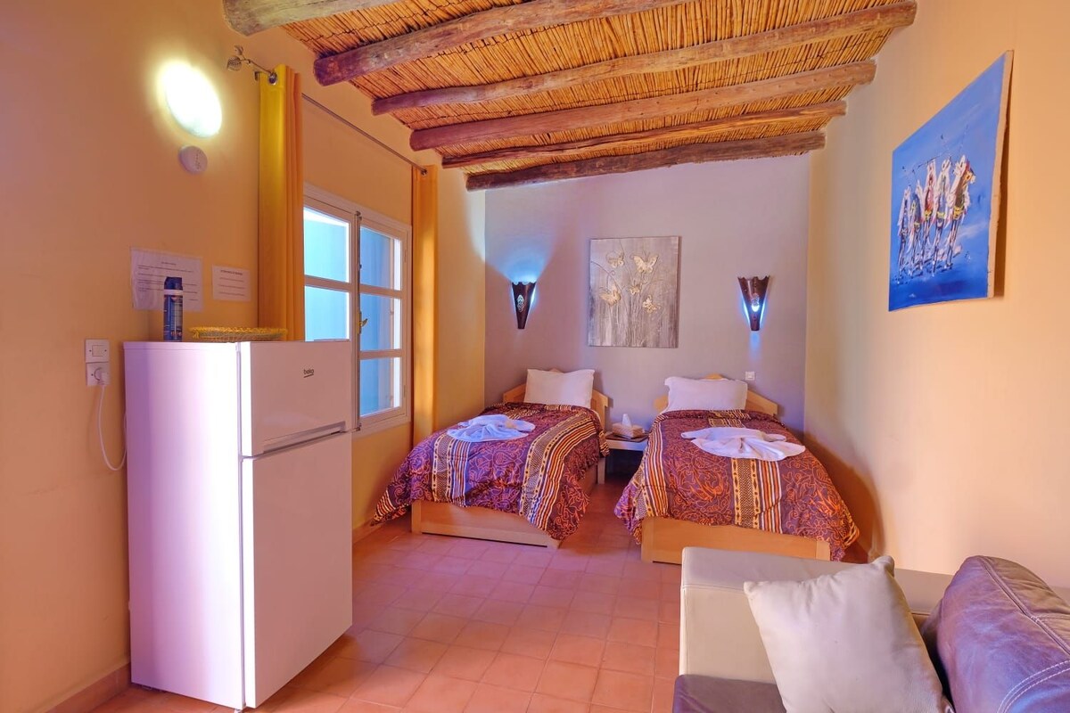 Una habitació amb dos llits, un frigorífic, una finestra i un quadre al mur.
