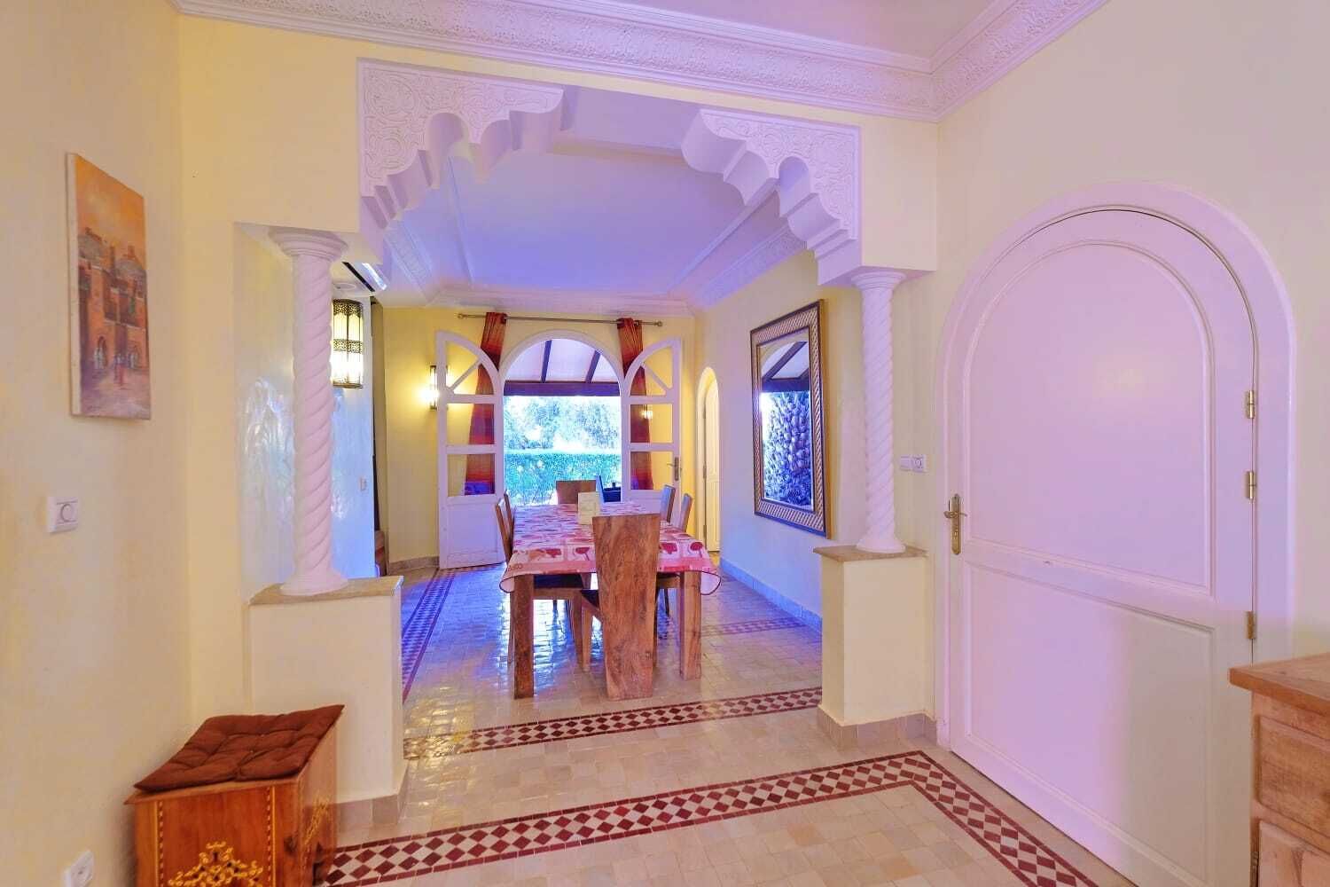 A hallway with a dining area, featuring a checkered floor, a table with chairs, and a door.