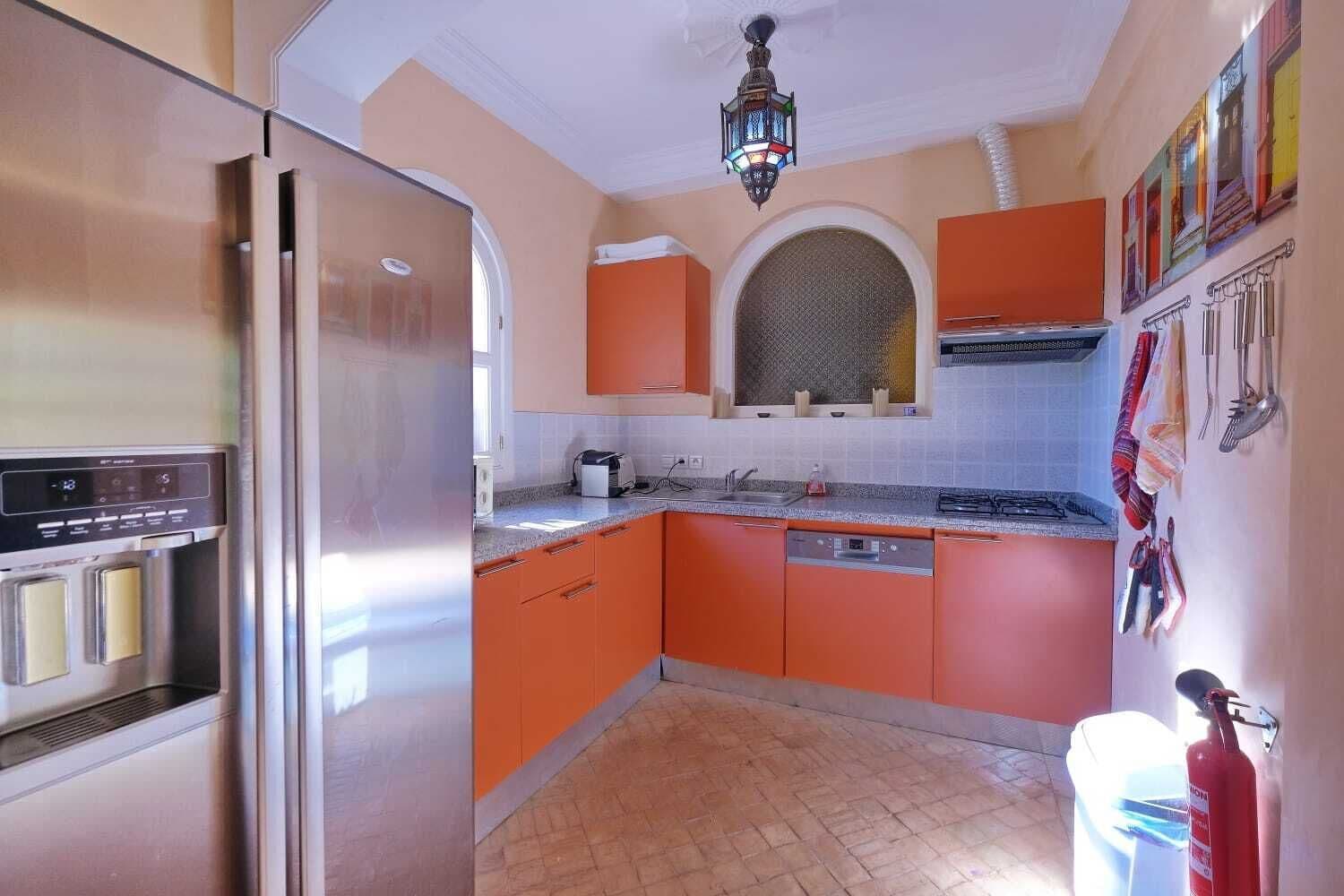 A kitchen with orange cabinets, a stainless steel refrigerator, a microwave, and a sink.