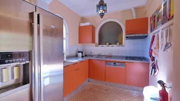 A kitchen with orange cabinets, a stainless steel refrigerator, a microwave, and a sink.