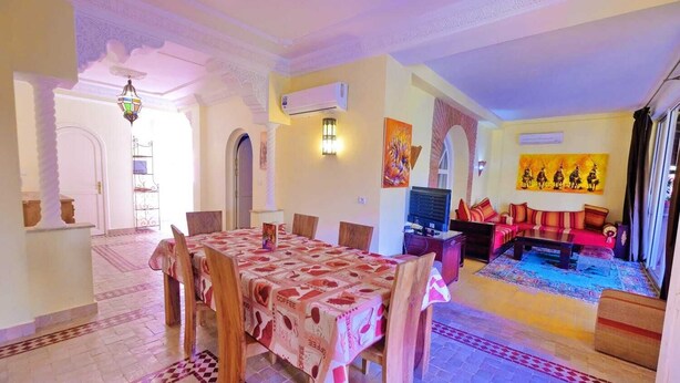 A dining area with a table set for four, a sofa, a television, and a painting on the wall.