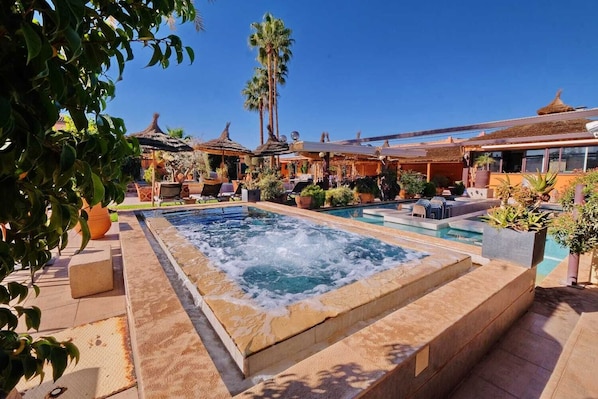 A pool area with a hot tub, lounge chairs, and palm trees.
