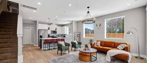 A modern living space with a staircase, a kitchen area, a sofa, and a dining table.