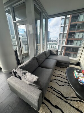 Ein modernes Wohnzimmer mit einem grauen Ecksofa, einem schwarzen Couchtisch und einem gemusterten Teppich.
