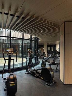 Ein modernes Fitnessstudio mit Cardiogeräten, großen Fenstern und einem eleganten Deckenstil.