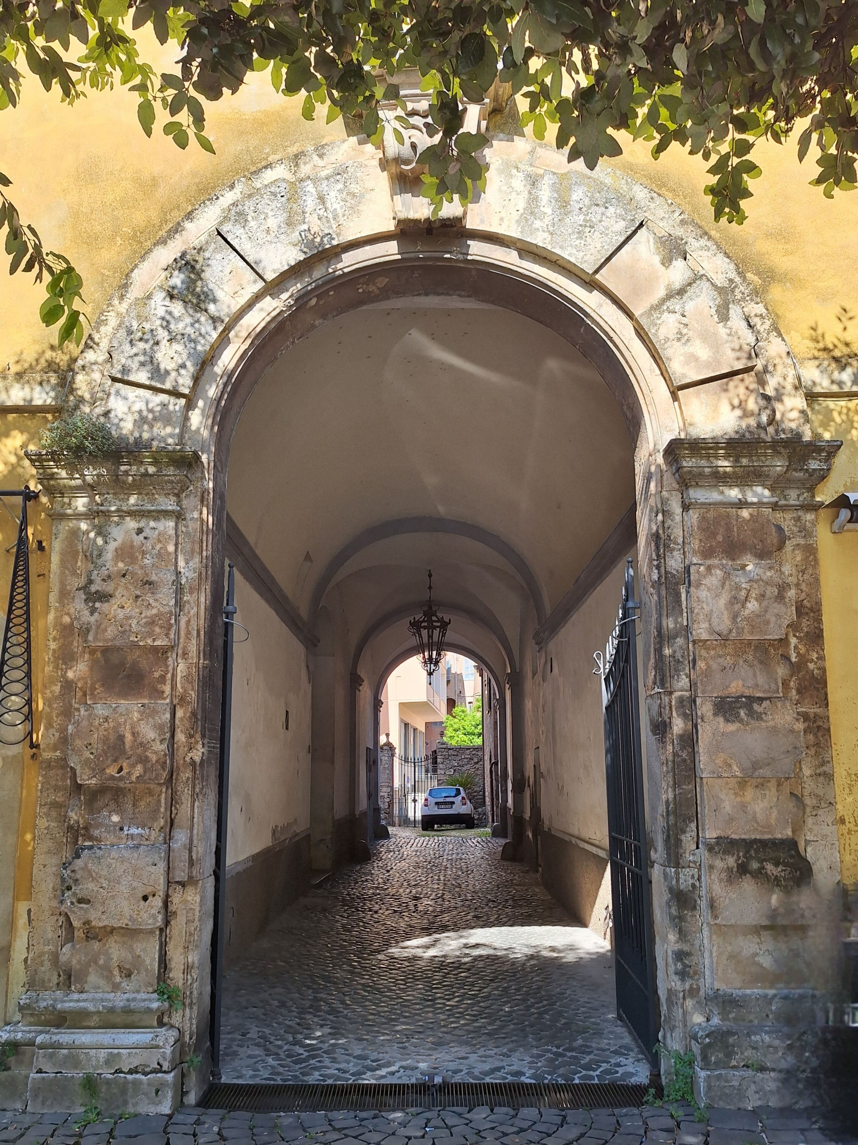 An arched stone corridor with a cobblestone floor leading to a gated entrance.