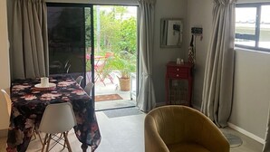 Amplia habitación con cama, una mesa de comedor con sillas, un sofá, una silla y una mesa de centro de vidrio. Cuenta con una puerta corrediza de vidrio que da a un espacio exterior con una mesa y sillas.