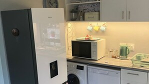 Une cuisine compacte équipée d’un réfrigérateur, d’un four à micro-ondes, d’un lave-linge et d’un évier.