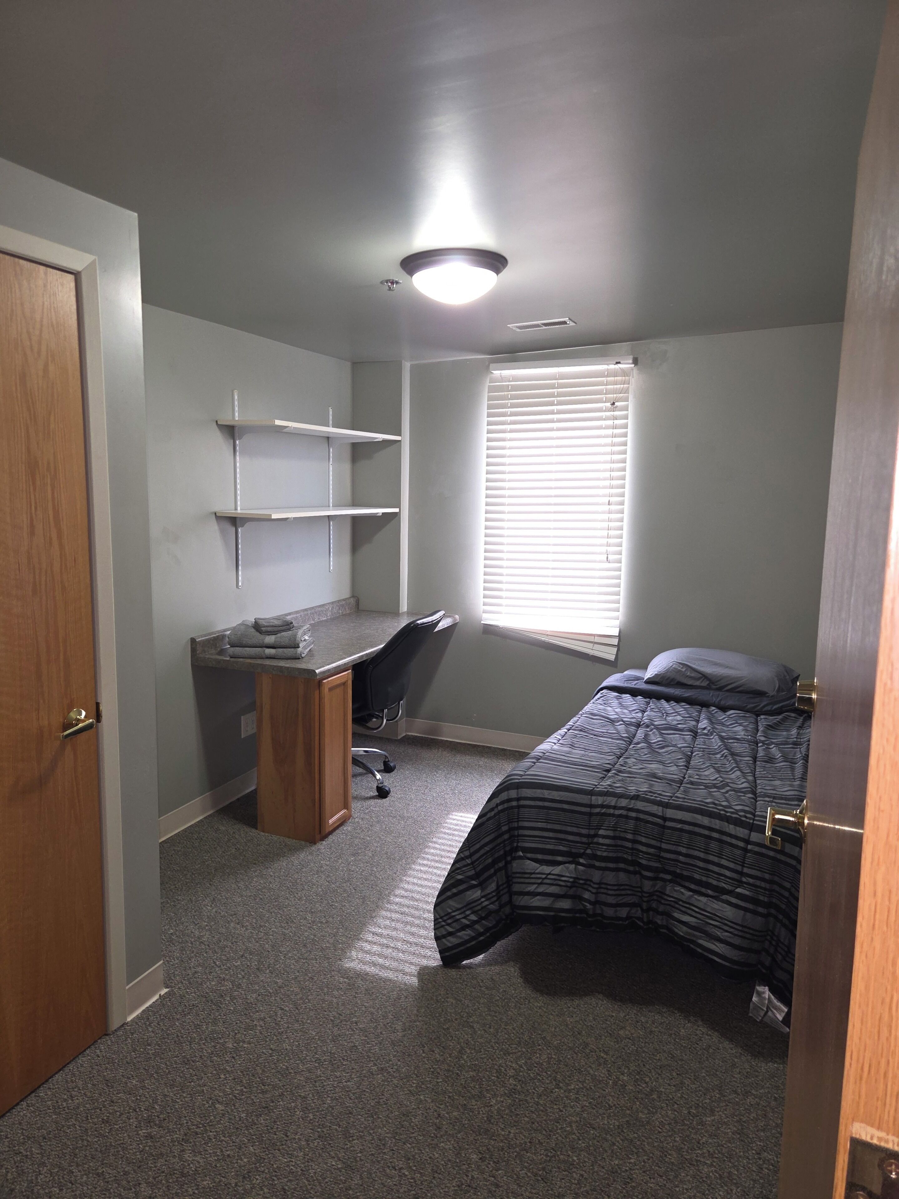 Une chambre à coucher comprenant un lit, un bureau, une chaise et des étagères intégrées.