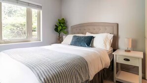 Una camera da letto con un letto, un comodino, una lampada e una finestra vista alberi.