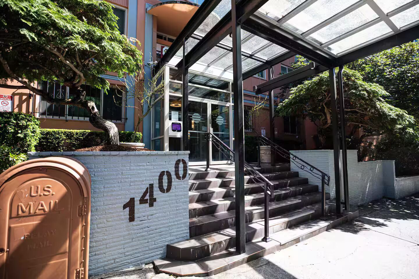 A building entrance with a glass canopy, a U.S. Mail mailbox, and a staircase leading to the entrance.