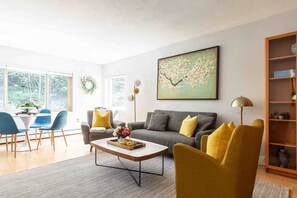 Ein modernes Wohnzimmer mit einem grauen Sofa, gelben Kissen, einem Couchtisch und einem Bücherregal.