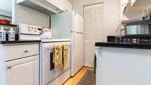Una cucina compatta con mobili bianchi, un piano cottura, un forno, un microonde e un frigorifero.