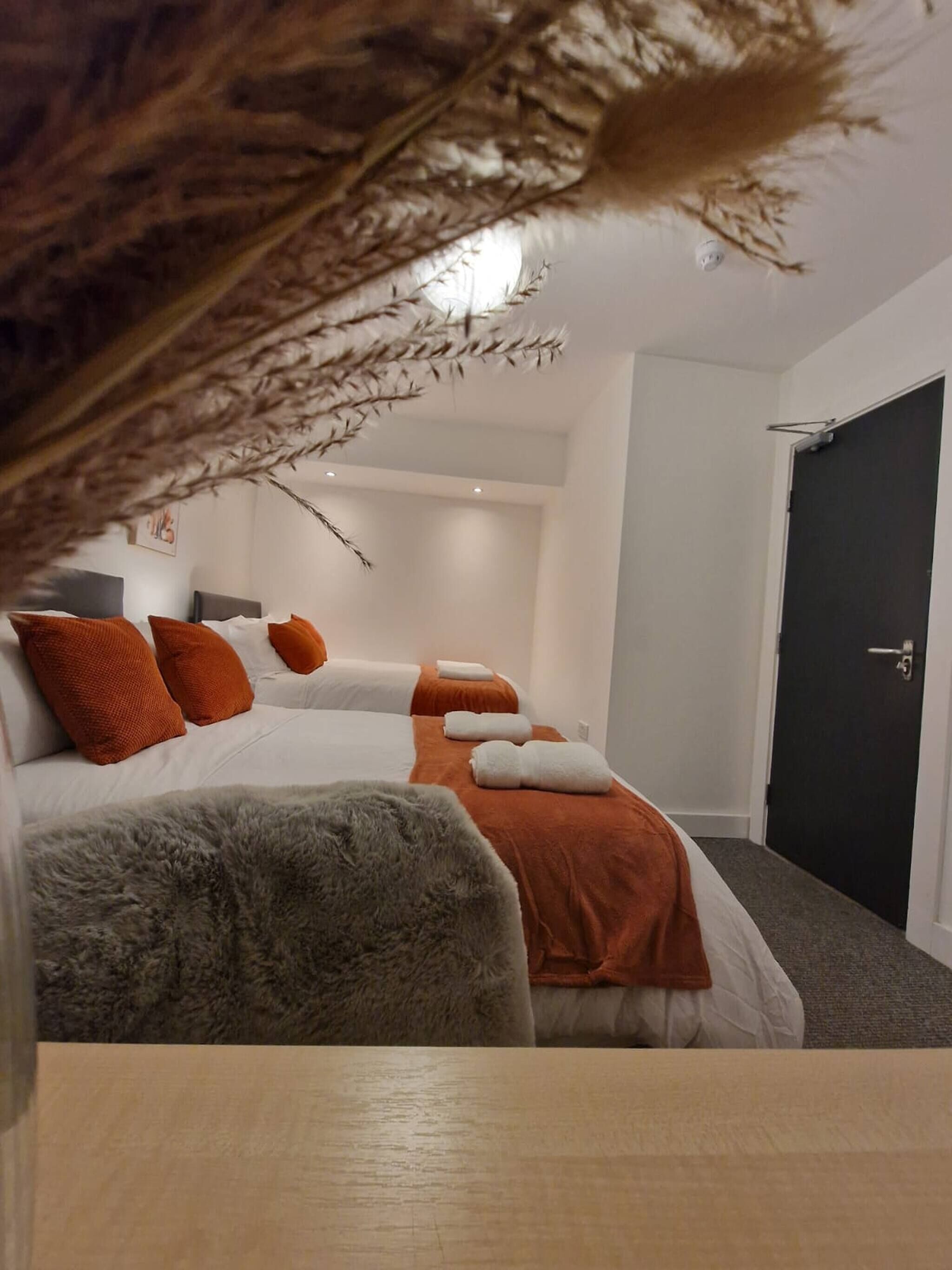 A hotel room with a bed, two pillows, a blanket, a fluffy chair, and a door.
