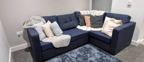 A living room with a dark blue sectional sofa, a grey shag rug, and three framed floral artworks on the wall.